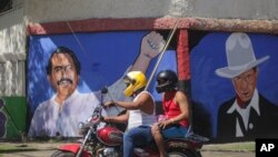 A motorcyclist rides past a mural of Nicaraguan President Daniel Ortega, left, and revolutionary hero Cesar Augusto Sandino during general elections in Managua, Nicaragua, Nov. 7, 2021.