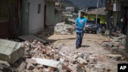 Seorang warga membawa satu galon air melewati jalan yang dipenuhi puing-puing bangunan yang roboh akibat gempa di San Pedro, Guatemala (7/7). (AP/Luis Soto)