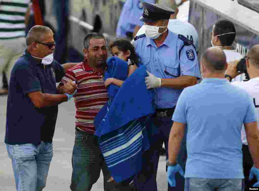 A rescued migrant cries as he carries his child to a police bus after disembarking from an Armed Forces of Malta (AFM) ship at the AFM Maritime Squadron base at Haywharf in Valletta's Marsamxett Harbor, Malta. Italian and Maltese naval vessels have recovered 34 bodies and rescued 206 people from a migrant boat which capsized while a rescue ship was dispatched to help another boat in distress, the Italian Navy said.