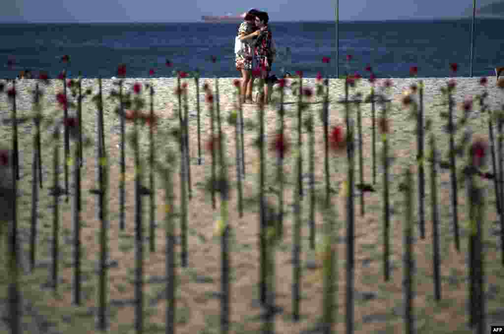People hug behind roses placed by the NGO Rio de Paz on Copacabana beach, Rio de Janeiro, in memory of Brazil's half a million COVID-19 victims.