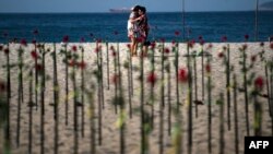 Para aktivis menancapkan 500 bunga mawar merah di Pantai Copacabana di Rio de Janeiro untuk mengenang 500.000 korban meninggal akibat pandemi virus corona di Brazil, hari Minggu (20/6) .