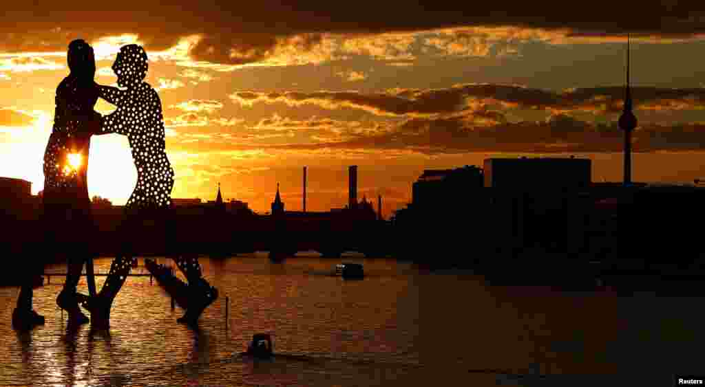 The sun sets behind the cityscape and the &quot;Molecule Men&quot;, a 30-meter-high sculpture by Jonathan Borofsky, located in Berlin&#39;s Spree river, Germany, Aug.7, 2016.