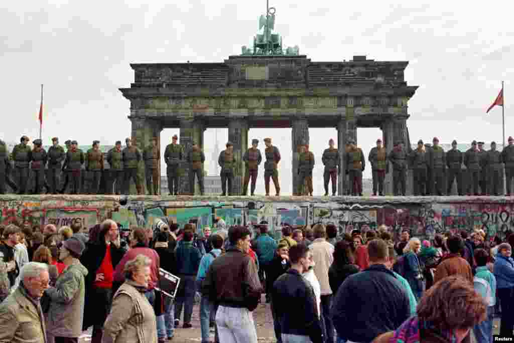 FILE PHOTO 11NOV89 - East Berlin border guards stand atop the Berlin Wall in front of the Brandeburg Gate in this November 11, 1989 file photo. The 10th anniversary off the "fall" of the Berlin wall is coming up on November 10, 1999. - RTXJABH