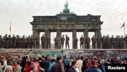 FILE - East Berlin border guards stand atop the Berlin Wall in front of the Brandeburg Gate on November 11, 1989.