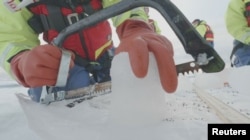 Seorang ilmuwan dari Proyek Northwest Passage pimpinan AS memotong inti es yang dibor dari Arktika Kanada dalam ekspedisi 18 hari pada Juli dan Agustus 2019. (Foto: Northwest Passage Project via Reuters)