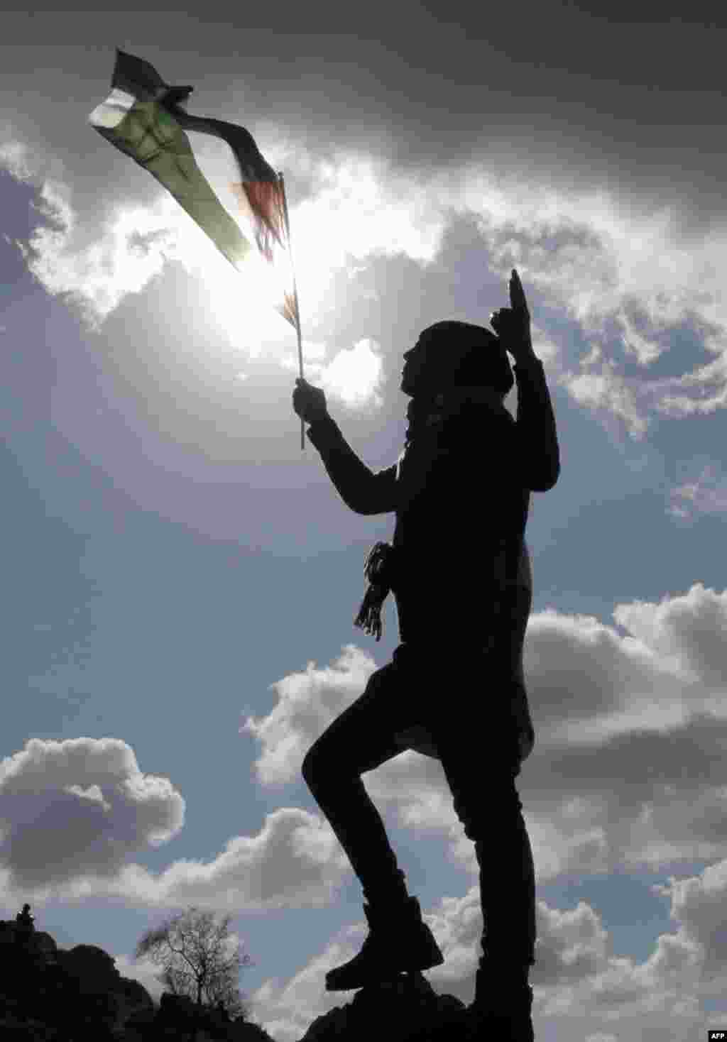 A Palestinian holds a flag on the top of a hill as demontrators set up a new camp to protest against Jewish settlements near the West Bank village of Burin.