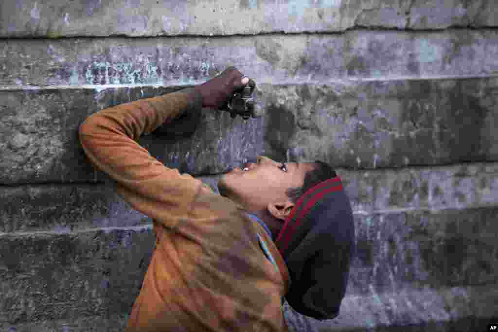 An Indian ragpicker boy drinks water from a tap at an automobile yard on the outskirts of Jammu, India.