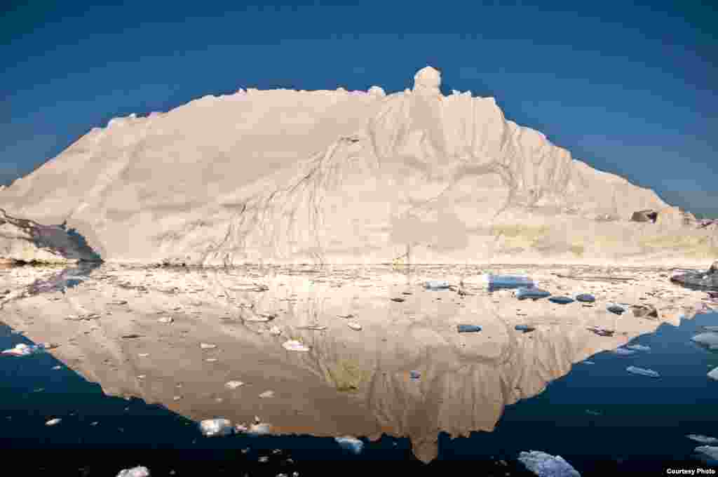 The midnight sun casts a golden glow on an iceberg and its reflection in Disko Bay, Greenland. Much of Greenland’s annual mass loss occurs through calving of icebergs such as this. (Photo courtesy Ian Joughin)