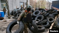 2014年4月12日一名武装人员在斯洛文斯克警察局外用轮胎堆成路障。
