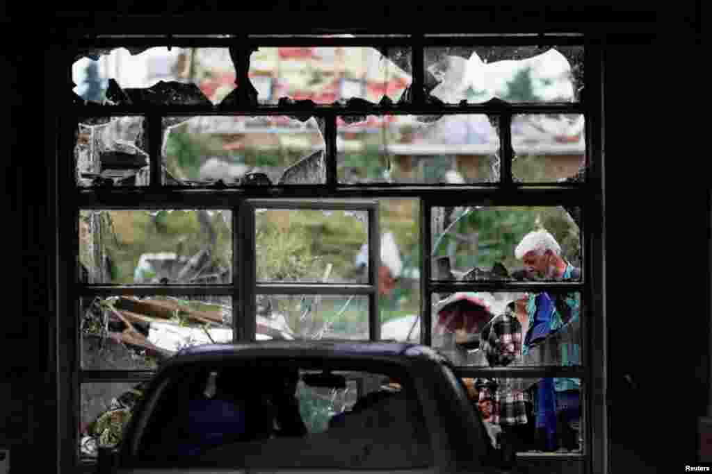 People are seen through a damaged window in the aftermath of a rare tornado that destroyed parts of some towns, in Mikulcice village, Czech Republic.