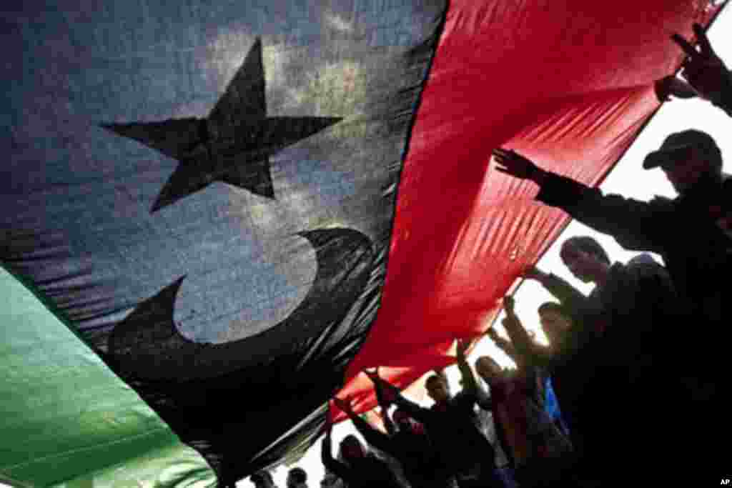Libyans hold a large pre-Gadhafi flag during a protest to demand the resignation of Libyan leader Moammar Gadhafi in Benghazi, eastern Libya, Wednesday, March 9, 2011.