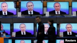 FILE - Visitors walk past TV sets during Russian President Vladimir Putin's live broadcast nationwide phone-in at the DNS electronic shop in Russia's Siberian city of Krasnoyarsk, April 17, 2014. Putin will take to live TV Thursday to try to fix some of the everyday problems of Russians.