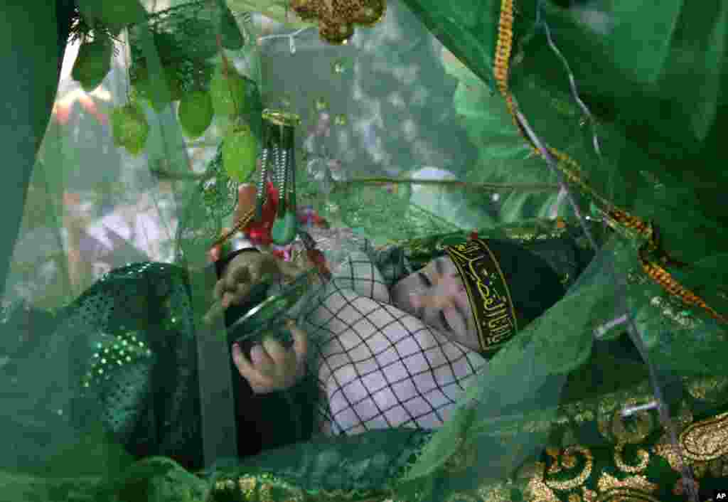 A Bahraini baby, laid for a blessing in a bassinet that is part of a living diorama, plays with ornaments, ahead of the Ashoura holiday during the month of Muharram, in Malkiya, Bahrain.