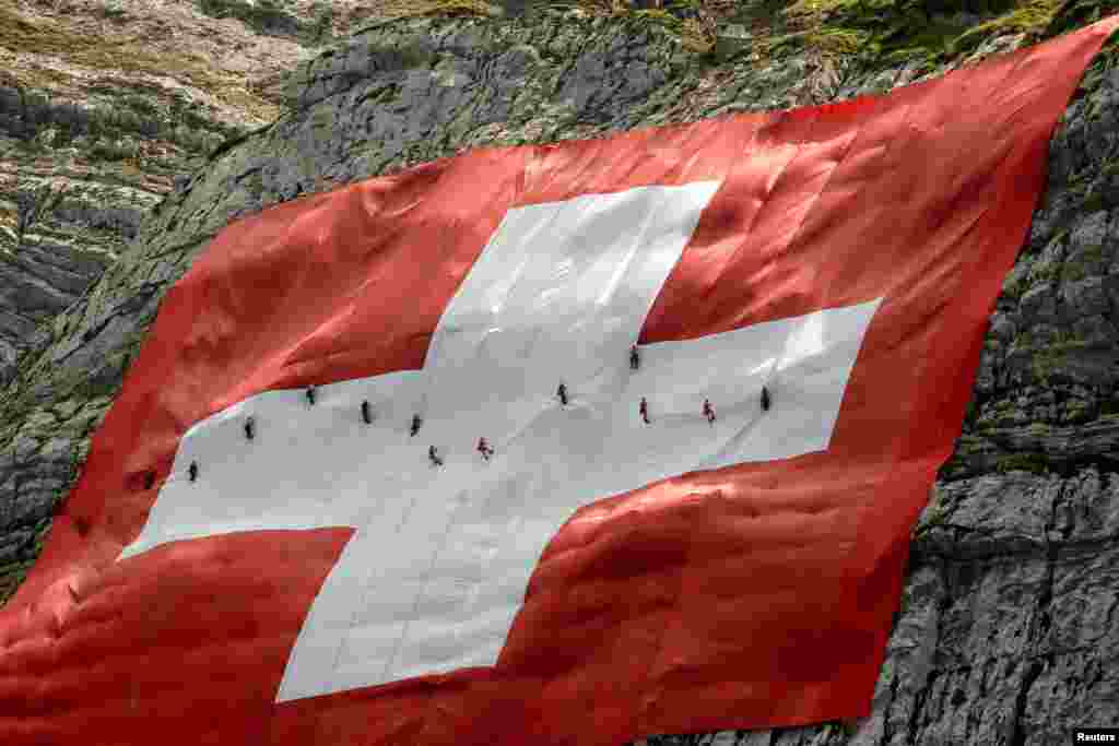 İsviçre&#39;nin kuzeydoğusundaki Saentis dağının batı yakasında 80x80 metre boyutundaki dev İsviçre bayrağını onaran dağcılar