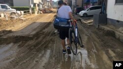 A man carries his bicycle on a mud-covered street in Hiroshima, southwestern Japan, Wednesday, July 11, 2018. 
