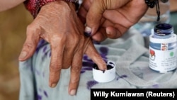 FILE - Seorang petugas pemilu membantu seorang perempuan lanjut usia untuk menandai jarinya dengan tinta setelah memberikan suaranya pada Pilkada di Tangerang, Banten, 27 Juni 2018. (Willy Kurniawan/REUTERS)