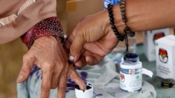 Seorang petugas pemilu membantu seorang perempuan lanjut usia untuk menandai jarinya dengan tinta setelah memberikan suaranya pada Pilkada di Tangerang, Banten, pada 27 Juni 2018. (Foto: Reuters/Willy Kurniawan)