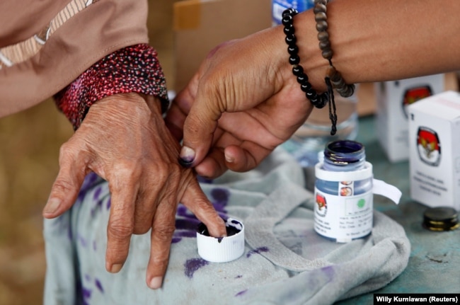 Seorang petugas pemilu membantu seorang perempuan lanjut usia untuk menandai jarinya dengan tinta setelah memberikan suaranya pada Pilkada di Tangerang, Banten, 27 Juni 2018. (Foto: REUTERS/Willy Kurniawan)