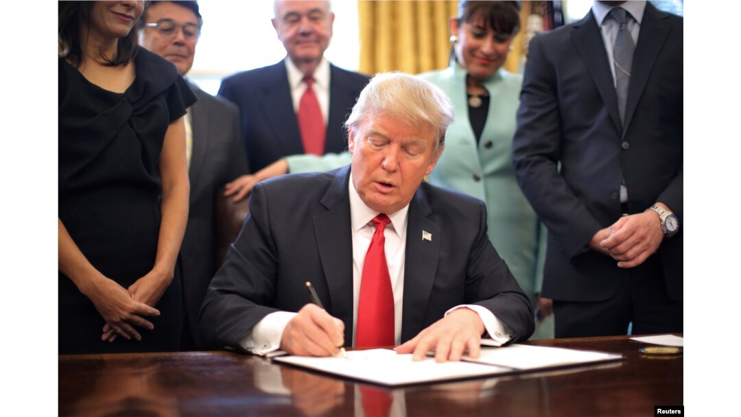 U.S. President Donald Trump signs an executive order cutting regulations, accompanied by small business leaders at the Oval Office of the White House in Washington, Jan. 30, 2017.