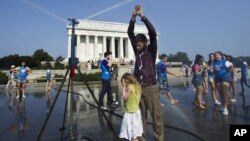 Visitors get some relief from a water sprinkler set up near the Lincoln Memorial in Washington, D.C., Saturday, July 7, 2012.