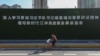 一名戴着口罩的妇女从武汉街头一幅宣传习近平湖北讲话的大标语前骑车而过。（2020年3月18日）