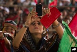 FILE - A woman uses her cell phone to take picture during a protest near the parliament building in Islamabad, Pakistan, Aug. 25, 2014.
