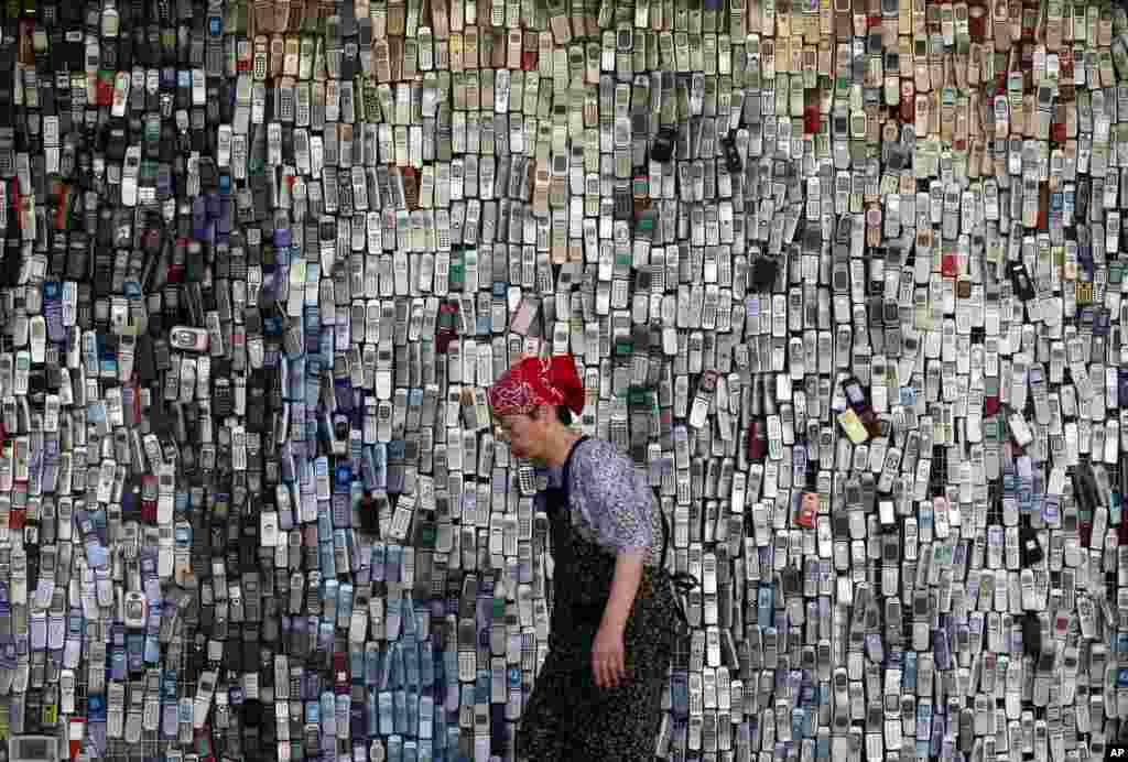 A woman walks past a wall of mock-up mobile phones displayed outside an electronics store in downtown Tokyo, Japan.