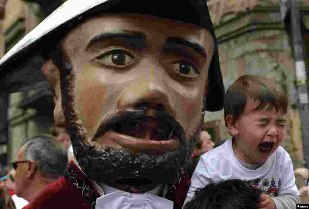 A child cries next to a &quot;Kiliki&quot; during the San Fermin festival&#39;s Comparsa de gigantes y cabezudos (Parade of the giants and the big heads) in Pamplona, Spain.