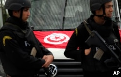 FILE - A Tunisian national flag is seen on a police vehicle as policemen stand guard following an attack by gunmen in Tunis, Tunisia, March 20, 2015.