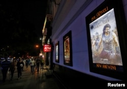 People walk past a poster of an Indian movie "Baahubali: The Beginning." "Baahubali 2" is in the works with more magical kingdoms and rampaging armies. .