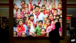 Seorang pengunjung berjalan melewati sebuah foto Presiden China Xi Jinping, dikelilingi oleh anak-anak, 28 September 2017.