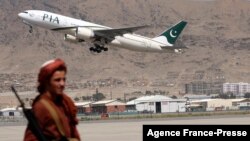 FILE - A Taliban fighter stands guard as a Pakistan International Airlines plane, the first commercial international flight to land after the Taliban retook power, takes off at the airport in Kabul on Sept. 13, 2021.