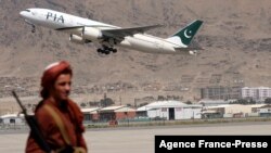 FILE - A Taliban fighter stands guard as a Pakistan International Airlines plane, the first commercial international flight to land since the Taliban retook power, takes off at the airport in Kabul on Sept. 13, 2021.