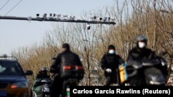 Security cameras overlook a street as vehicles pass under in Beijing, China on Nov. 25, 2021. The system will alert police and officials if people who have been grouped as a "risk" cross a border, or perform other activities. (REUTERS/Carlos Garcia Rawlins)