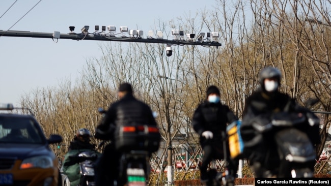 Security cameras overlook a street as vehicles pass under in Beijing, China on Nov. 25, 2021. The system will alert police and officials if people who have been grouped as a "risk" cross a border, or perform other activities. (REUTERS/Carlos Garcia Rawlins)