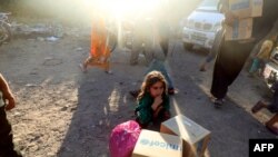 Seorang anak pengungsi dari Suriah yang melarikan diri dari Raqa, berada di belakang kotak bantuan kemanusiaan yang diserahkan oleh UNICEF di sebuah kamp sementara di kota Tabqa, sekitar 55 kilometer (35 mil) barat Raqa.