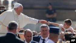 Paus Fransiskus menyambut uluran tangan seorang anak pada acara pertemuan publik mingguan di Vatikan, Rabu (19/6). 