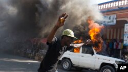 Un protestataire passe devant une voiture en feu lors d'une manifestation contre le gouvernement du président Michel Martelly à Port-au-Prince, en Haïti, le 18 janvier 2016.