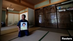 FILE - Mikio Watanabe holds a portrait of his late wife Hamako at his home at Yamakiya district in Kawamata town, Fukushima prefecture, June 23, 2014.