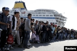 FILE - Refugees and migrants line up to board buses at the Greek port of Piraeus, near Athens, Oct. 15, 2015.