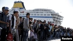 Refugees and migrants line up to board buses at the Greek port of Piraeus, near Athens, Oct. 15, 2015. They were among nearly 2,500 arriving from Lesbos on the passenger ferry, Eleftherios Venizelos. 