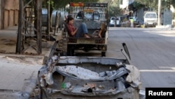 Men rest at the back of a pickup truck near a damaged car in the rebel held al-Katerji district in Aleppo, Syria, Aug. 13, 2016. 