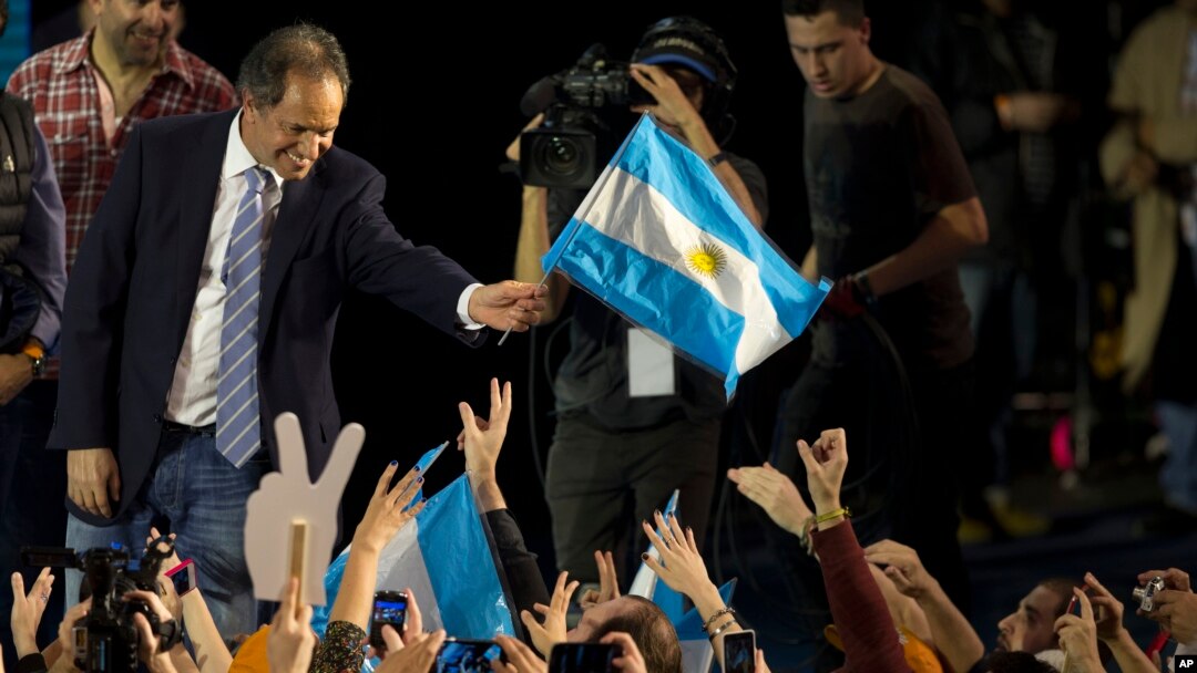 FILE - Ruling party presidential candidate Daniel Scioli, a no-show at the debate, holds an Argentine flag as he acknowledges supporters after primary elections in Buenos Aires, Argentina, Aug. 10, 2015.