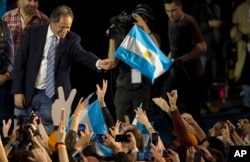 FILE - Ruling party presidential candidate Daniel Scioli holds an Argentine flag as he acknowledges supporters after primary elections in Buenos Aires, Argentina, Aug. 10, 2015.
