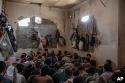 FILE - More than 100 Islamic State suspects sit inside a small room in a prison south of Mosul, July 18, 2017.