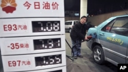 A taxi driver looks at the price as he fills the tank of his car near a board showing recently increased prices at a gas station in Shenyang, Liaoning province, February 20, 2011.