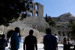 Turis mengambil foto teater Herodes Atticus dan kuil Parthenon di atas bukit Acropolis di Athena. (Foto: AP)