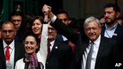 The first elected female mayor of Mexico City Claudia Sheinbaum and President Andres Manuel Lopez Obrador lift their arms in unison after she was sworn into office, in Mexico City, Dec. 5, 2018. 