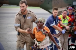 People are escorted to safety by aid workers at the airport of the coastal city of Beira in central Mozambique on March 19, 2019, after the area was hit by the Cyclone Idai.