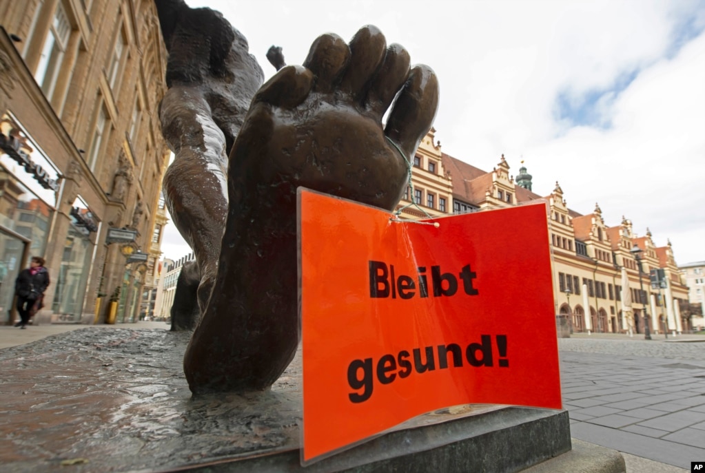 Un letrero que dice "Manténgase saludable" cuelga de la escultura "El paso del siglo", de Wolfgang Mattheuer, en Leipzig, Alemania.